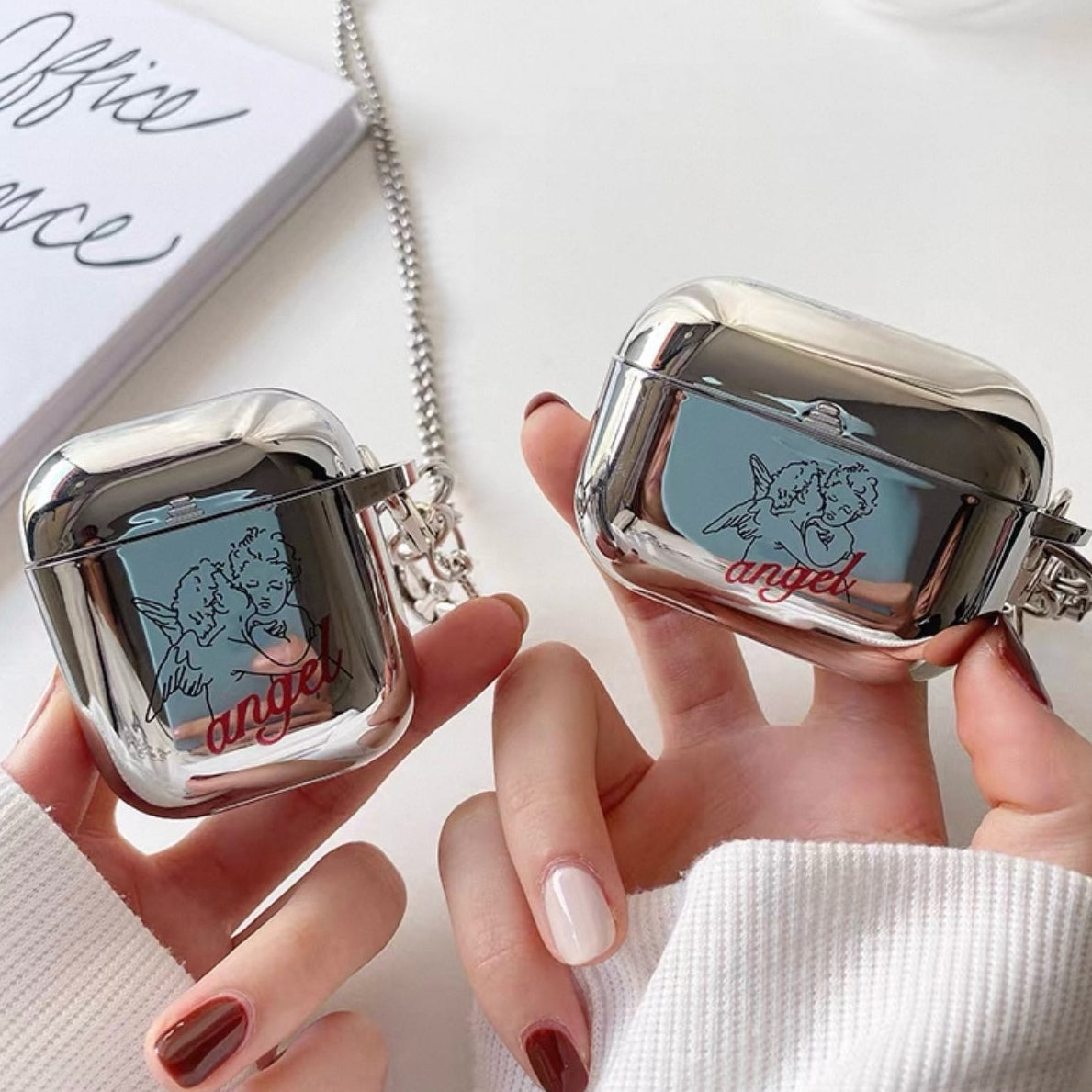 Brisconti Portofino AirPods-Schutzhülle in glänzendem Silber mit Engel-Motiv, rotem Schriftzug und silberner Kette.