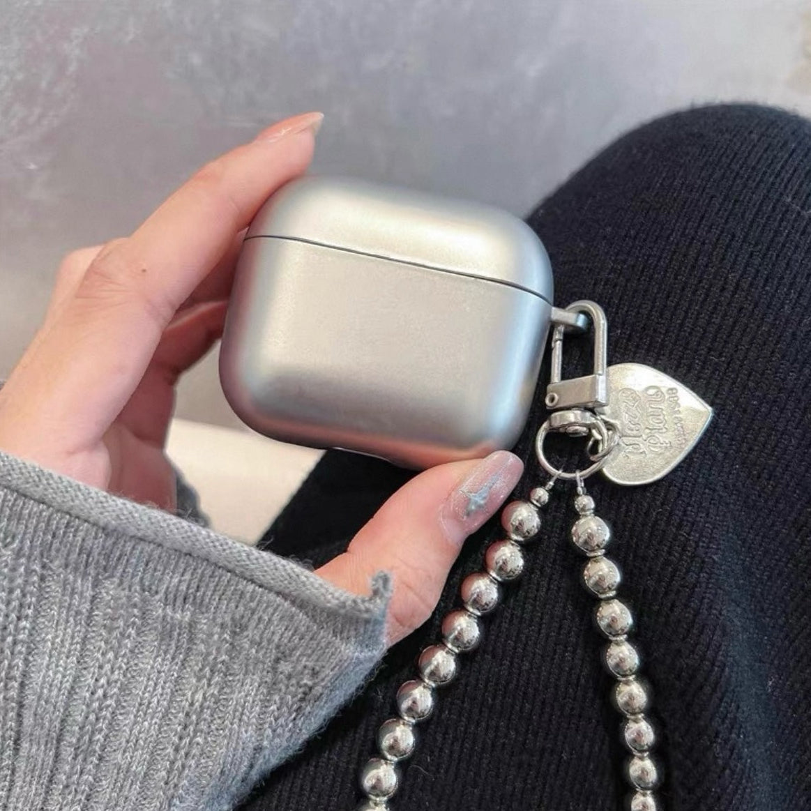 Brisconti Portofino silbernes AirPods-Case mit Perlenarmband und Herz-Anhänger in einer Hand gehalten